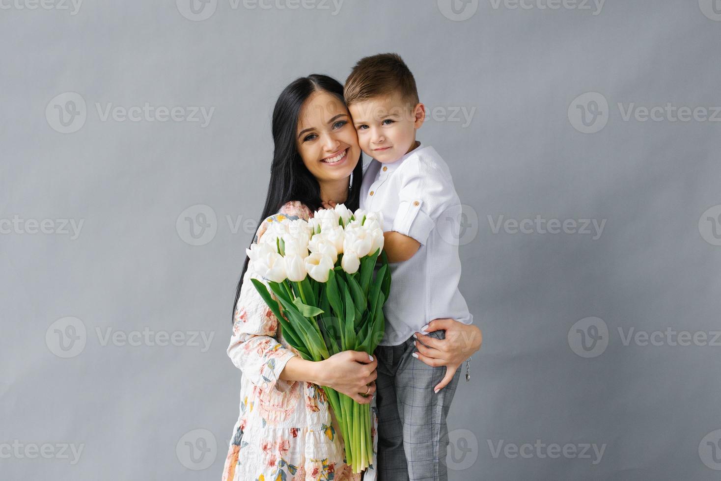 ritratto di un' giovane madre con un' mazzo di bianca tulipani e un' giovane figlio avendo divertimento. famiglia, affascinante bambino, il concetto di amore e felicità foto
