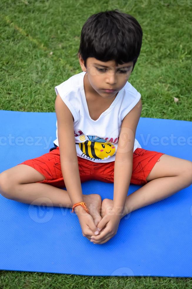 asiatico inteligente ragazzo fare yoga posa nel il società parco all'aperto, figli di yoga posa. il poco ragazzo fare yoga esercizio. foto