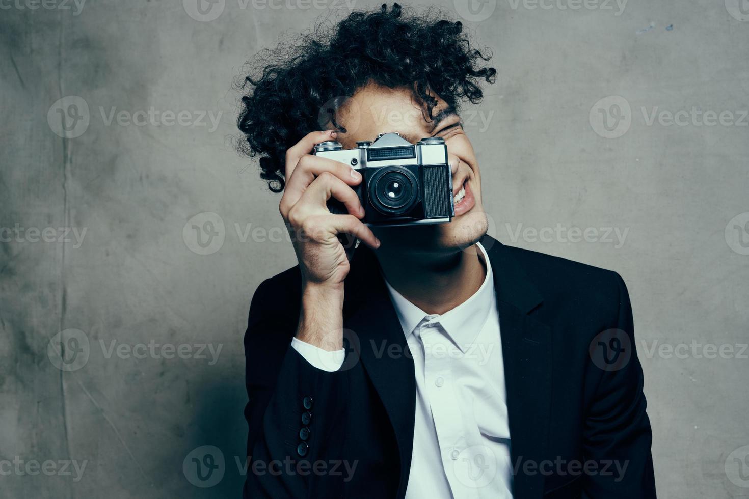 fotografo con un' telecamera nel un' classico completo da uomo Riccio capelli studio modello foto