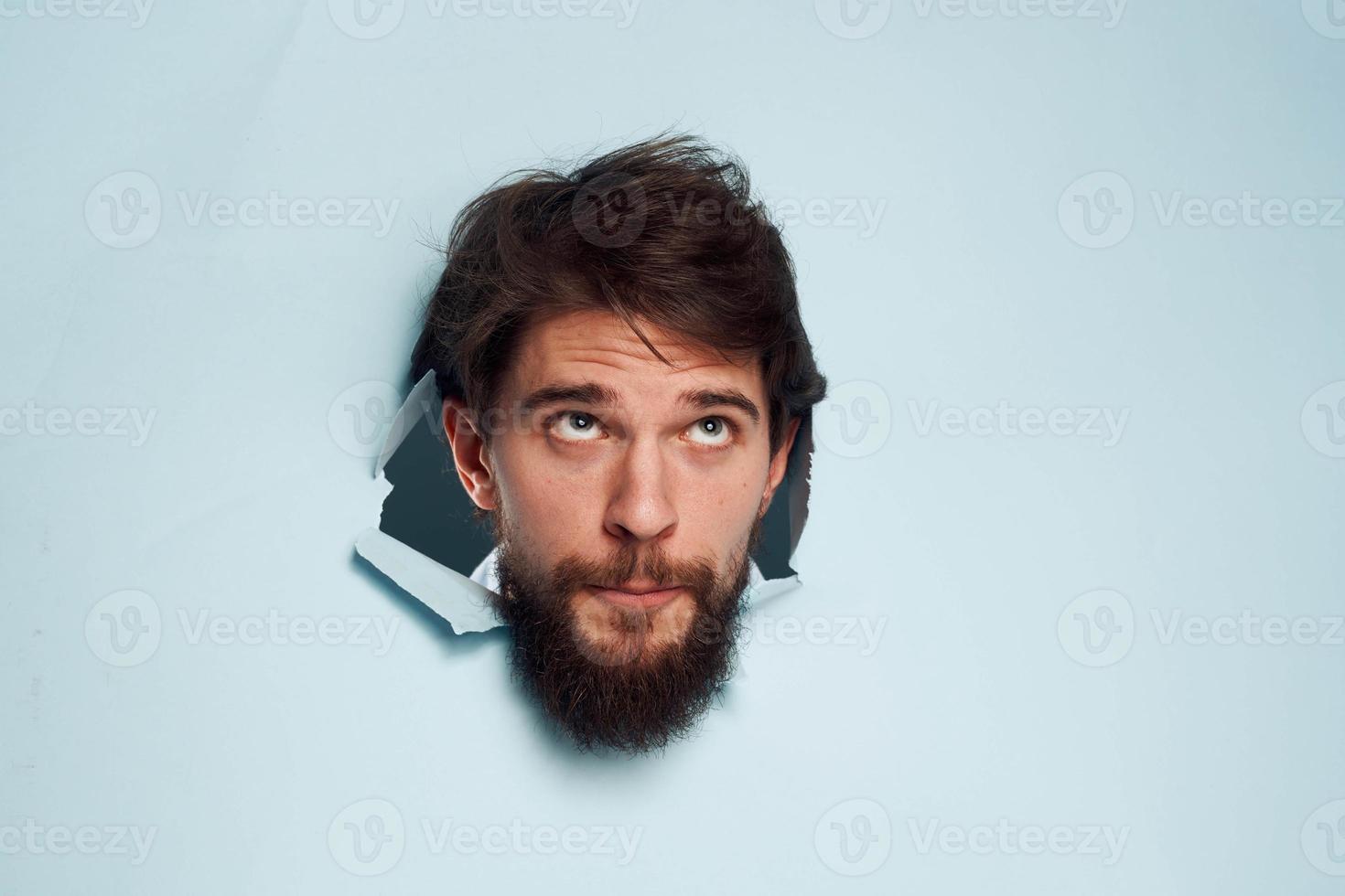 emotivo uomo fa capolino il suo testa su di il blu sfondo parete foto