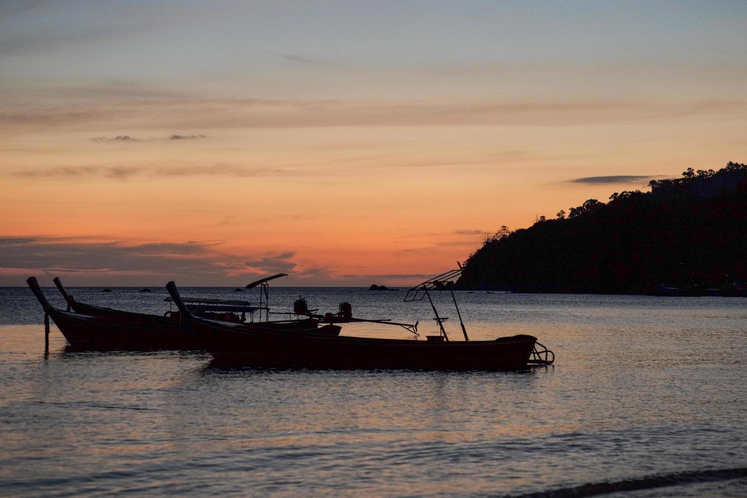 silhouette gruppo di tradizionali barche a coda lunga galleggianti nel mare con il crepuscolo del tramonto e l'isola sullo sfondo foto