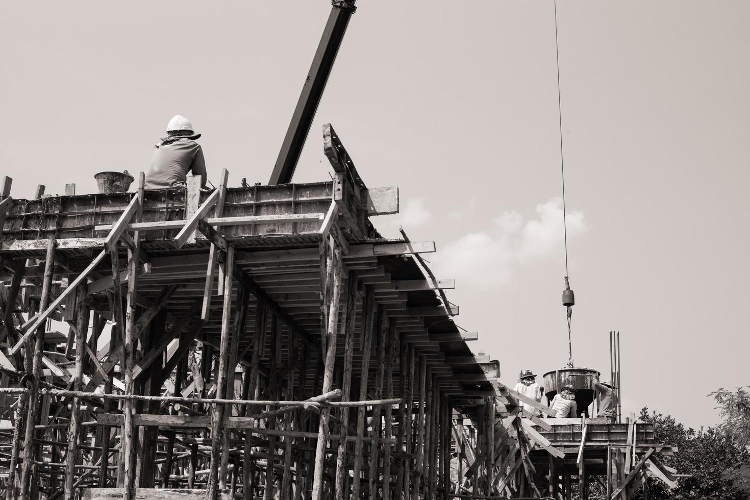 monocromatico dei lavoratori che trasportano il contenitore di cemento da versare in cantiere foto