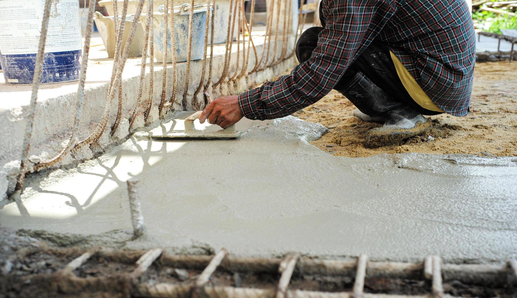 lavoratore utilizzando una spatola di legno per il livellamento del pavimento in cemento foto