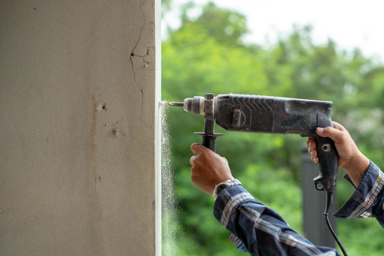 primo piano le mani del lavoratore tiene un trapano elettrico e trapani nel muro di cemento foto