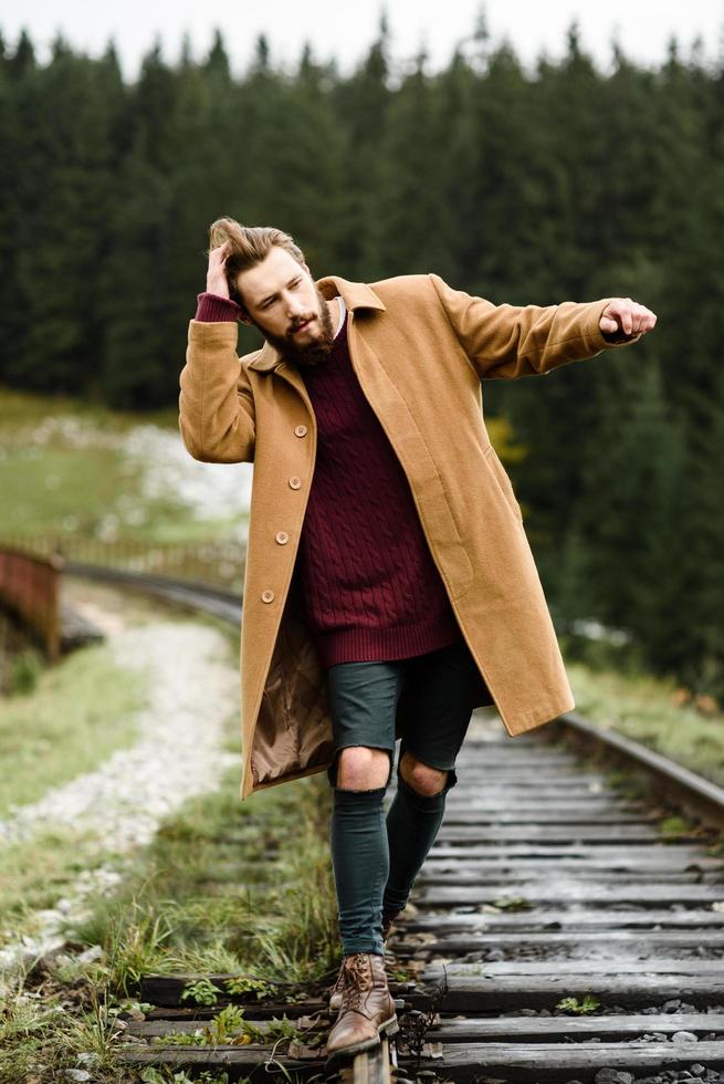 uomo barbuto brutale cammina sui binari nei Carpazi, sullo sfondo alti abeti foto