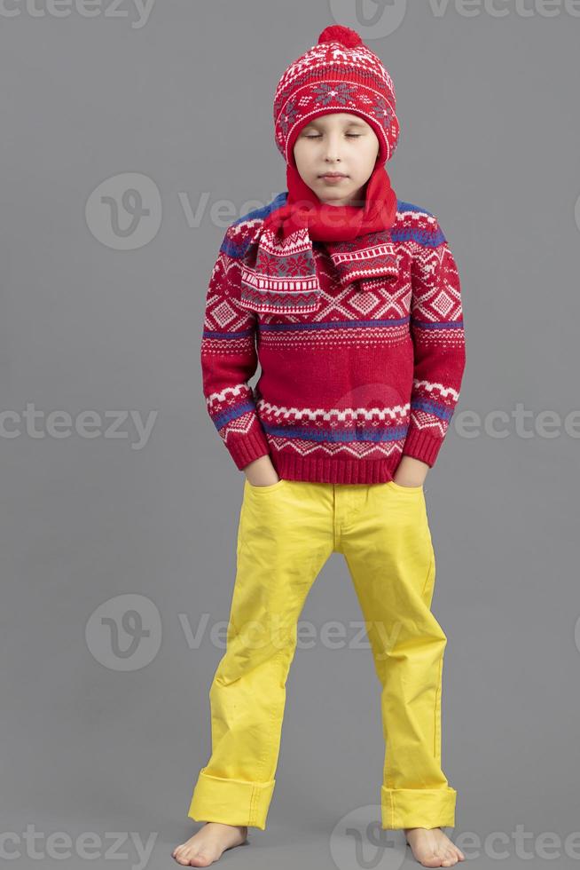 un' bambino nel caldo Abiti. ragazzo nel un' inverno cappello, sciarpa e rosso maglione a piedi nudi. alla moda ragazzo nel il studio. foto