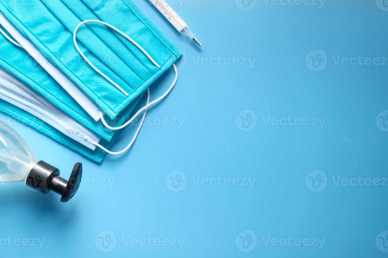 maschere chirurgiche, termometro e disinfettante per le mani su sfondo blu foto