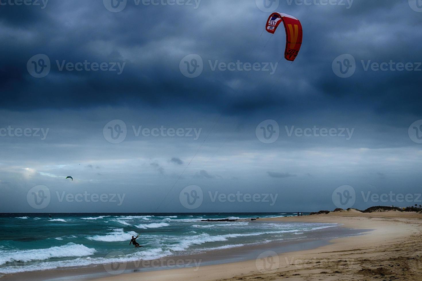 estate paesaggio con il oceano con buio nuvoloso onde e surfermi kit con paracadute galleggiante su il riva foto