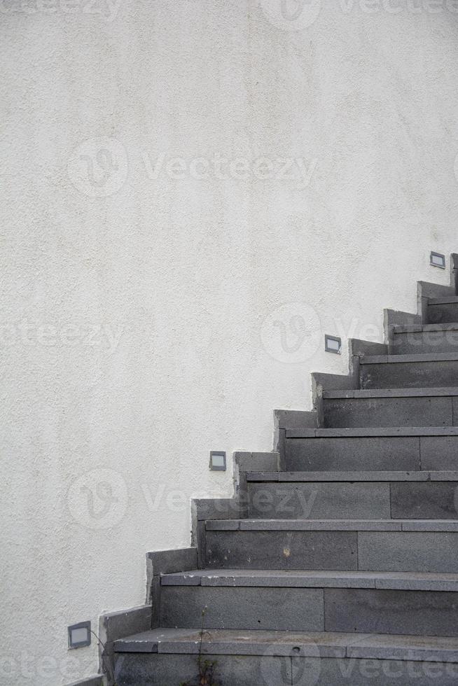 il scala su il bianca parete di il edificio nel il parco, il grigio pietra scala su il bianca cemento parete sfondo. foto