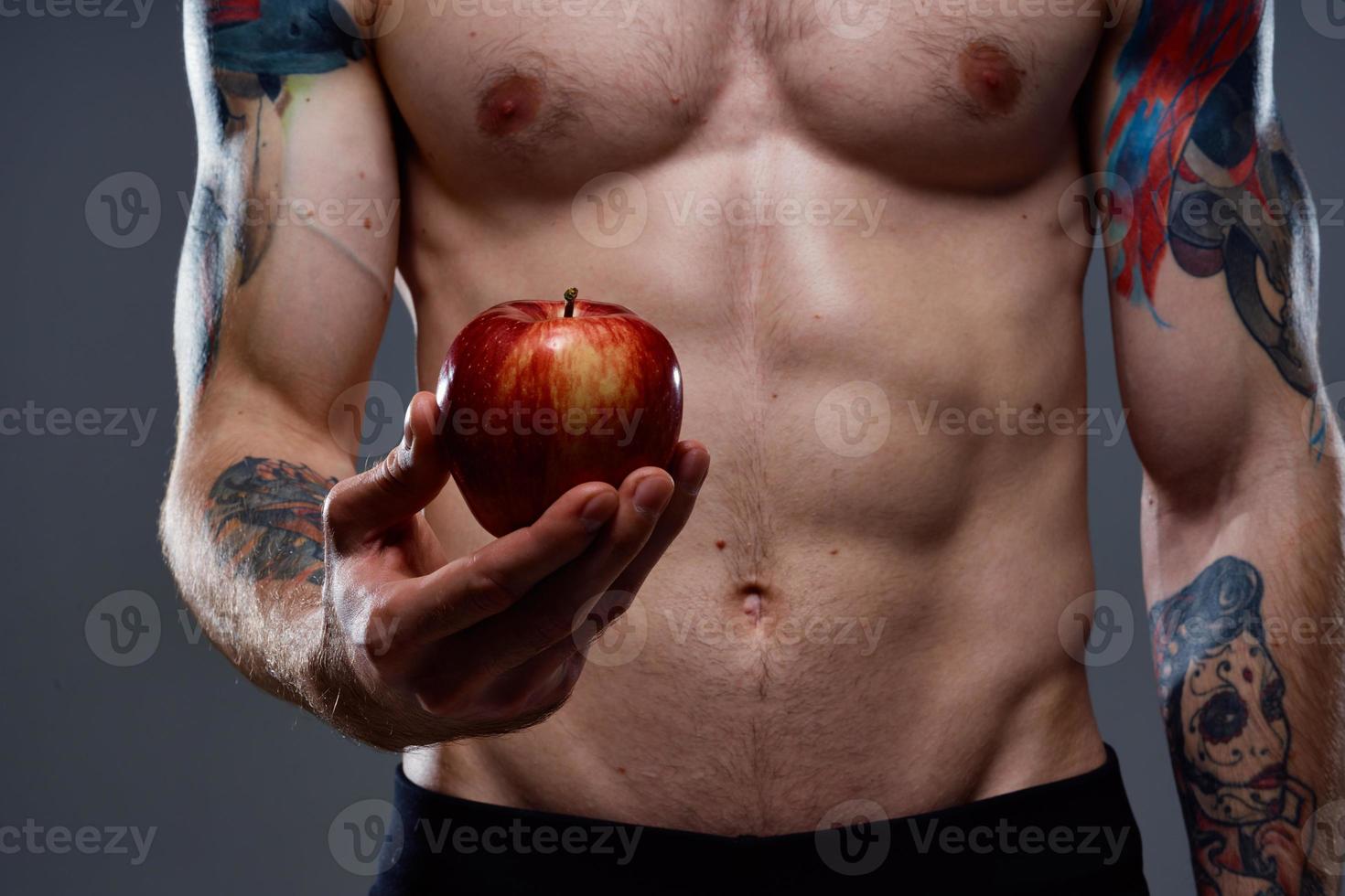 nudo bodybuilder con pompato muscoli e tatuaggio Mela nel mano Salute foto