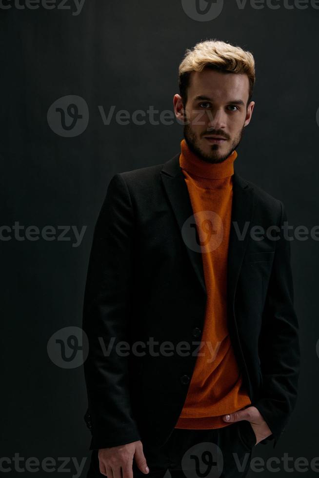 biondo uomo nel un' cappotto e un arancia maglione su un' buio sfondo davanti Visualizza modello foto