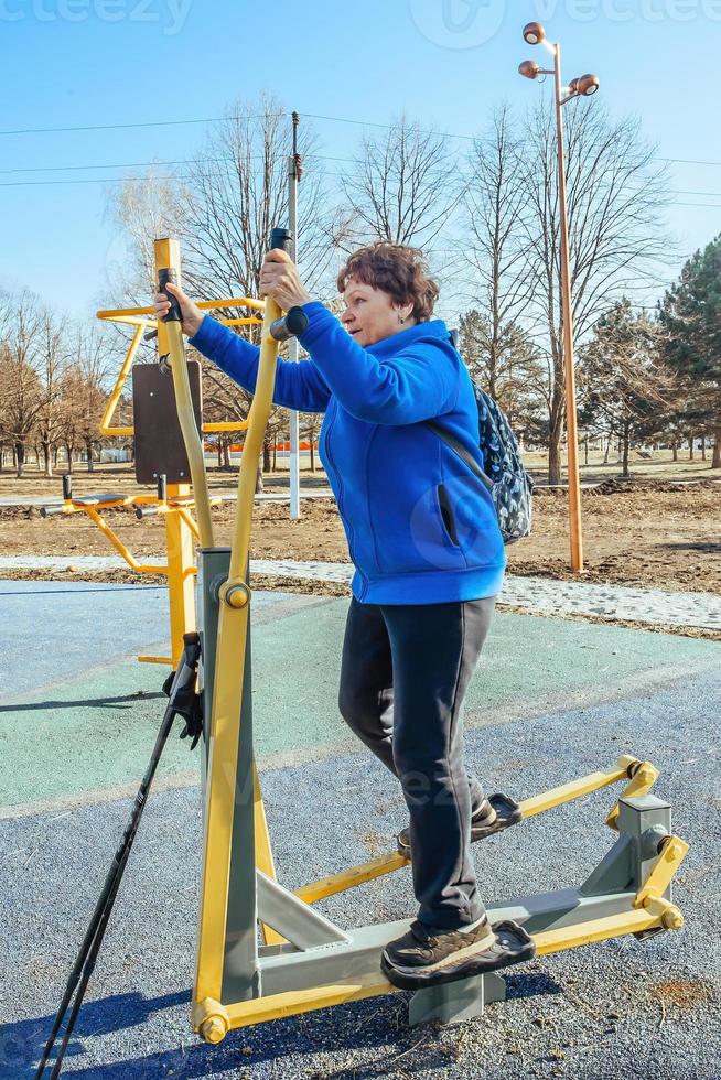 un' pensionato donna con un' zaino su sua le spalle su un attivo camminare all'aperto è impegnato nel esercizio attrezzatura nel il parco. anziano donna assunzione cura di sua Salute foto