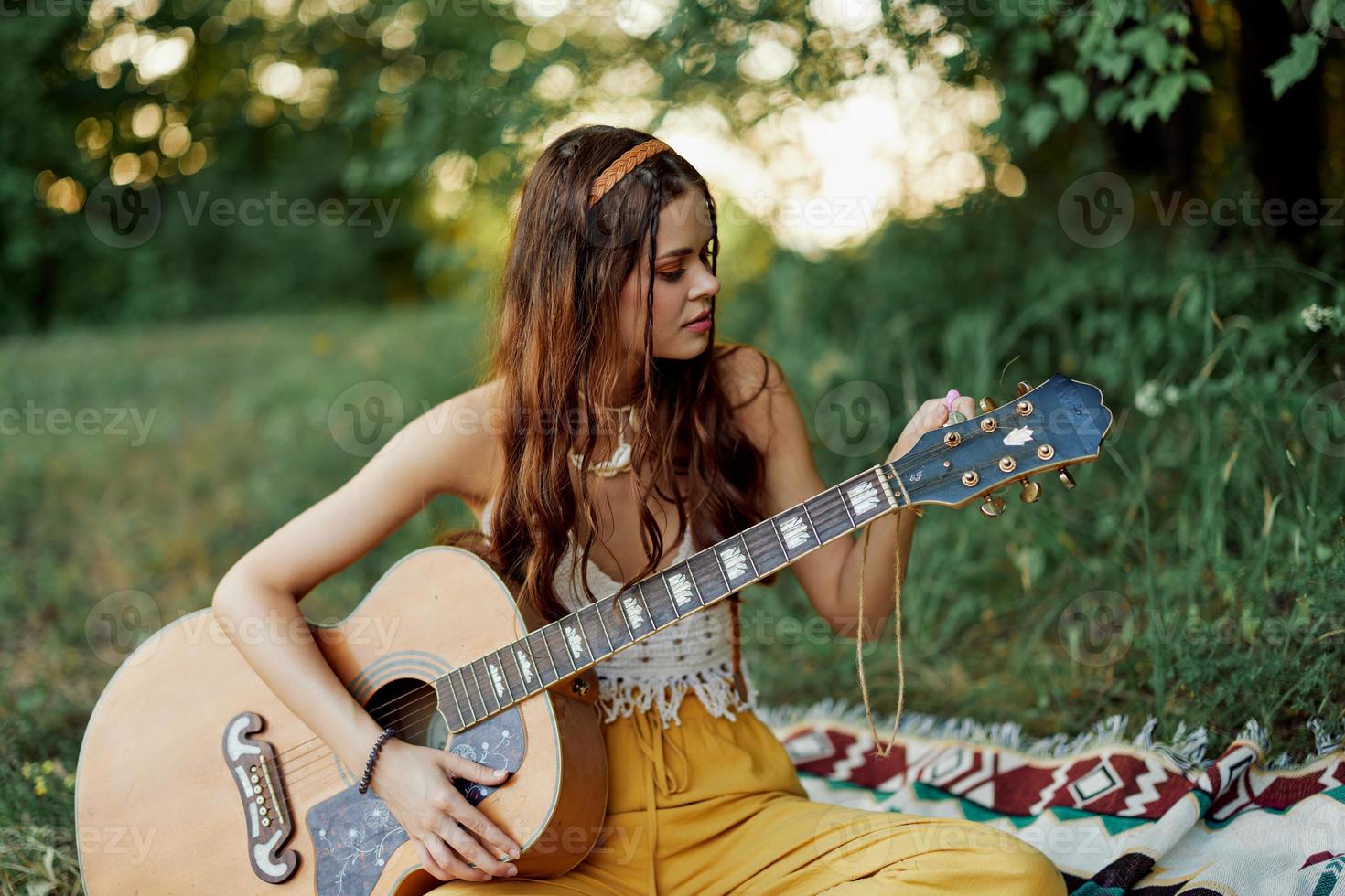 contento hippie donna con un' chitarra sorrisi seduta nel natura di il lago foto