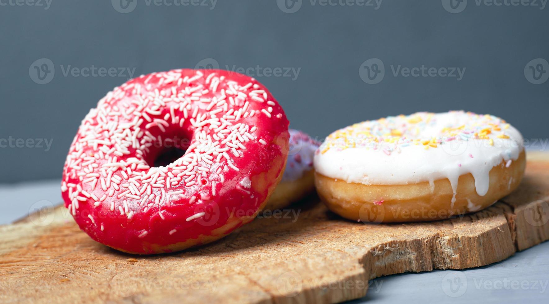 tre ciambelle glassate assortite su una tavola di legno e uno sfondo grigio foto