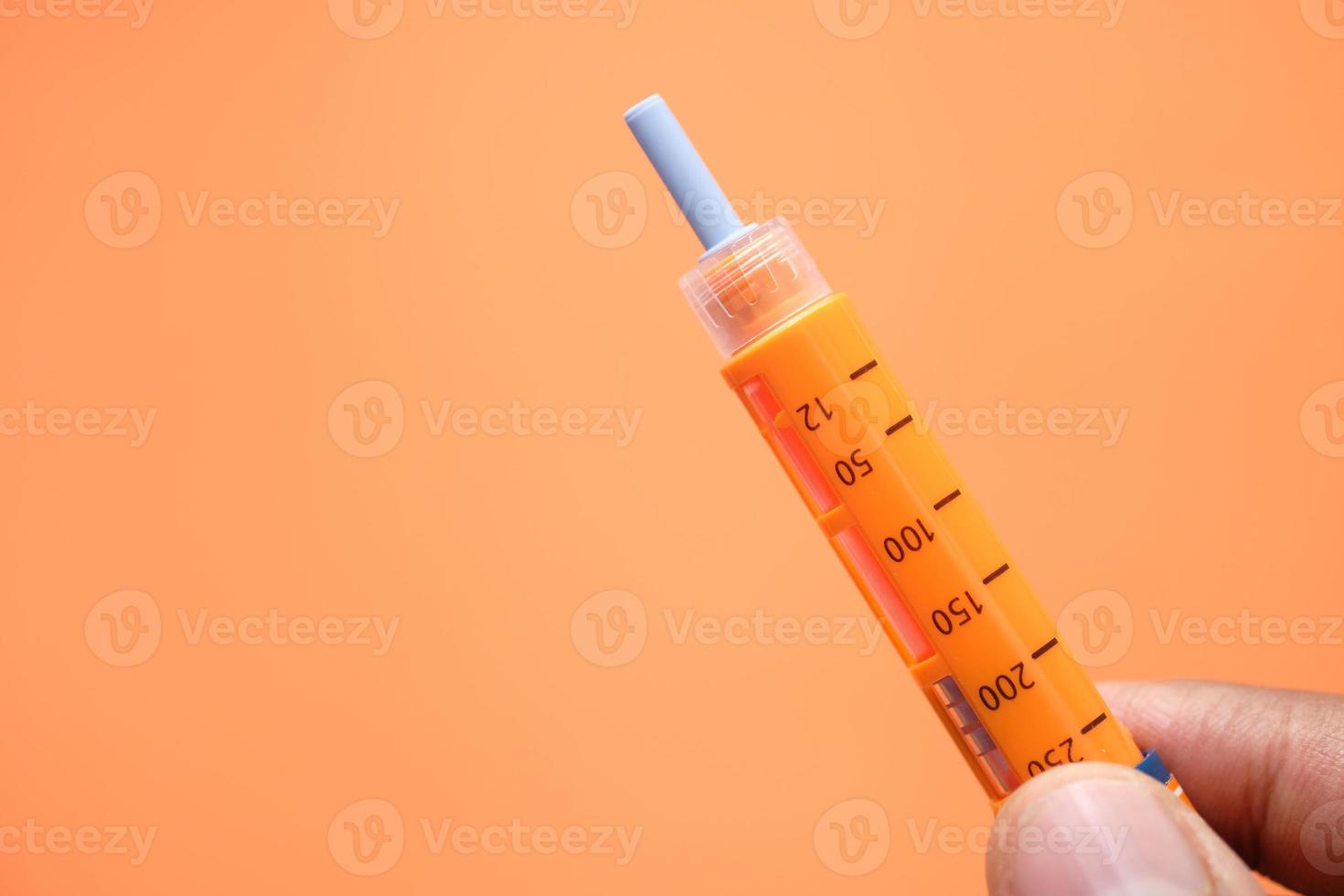 mano che tiene la penna per insulina con copia spazio arancione foto