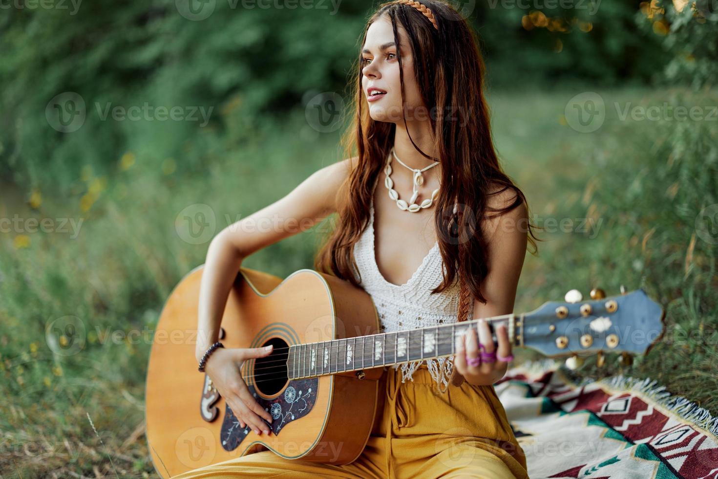 hippie donna sorridente e abbracciare sua chitarra nel natura nel il parco nel il tramonto leggero nel eco-abbigliamento foto