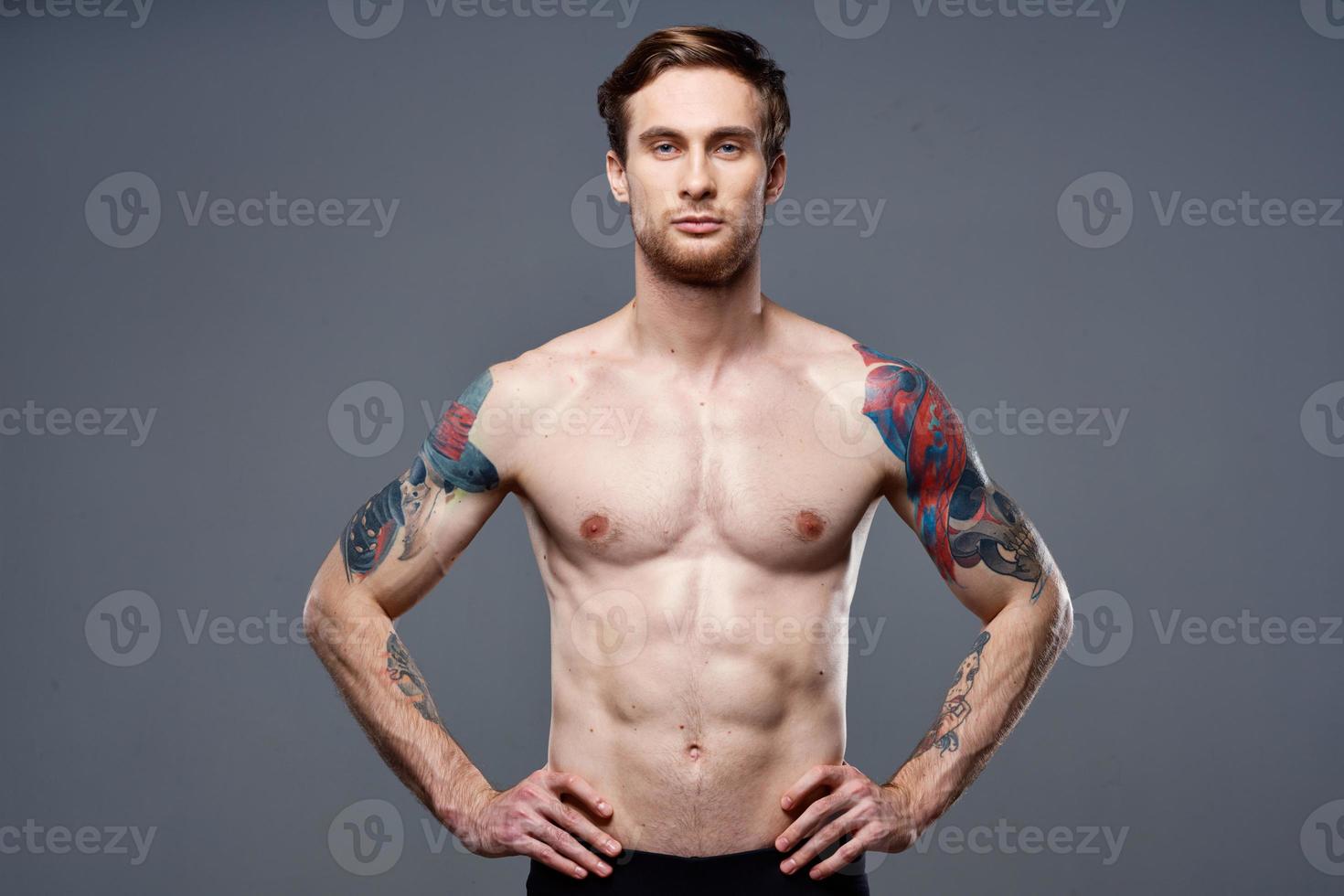 sportivo uomo tatuaggi su il suo braccia nudo torso bodybuilder grigio sfondo foto