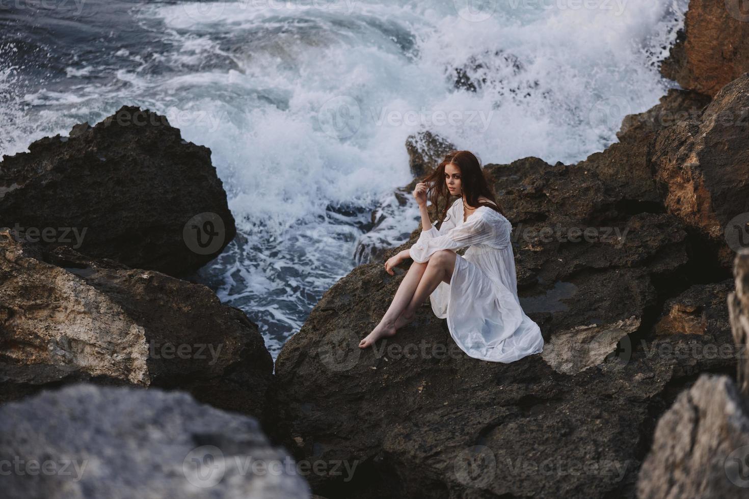 bellissimo donna nel bianca vestito bagnato capelli pietra spiaggia nuvoloso tempo metereologico foto