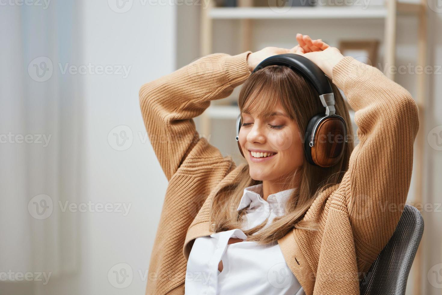 contento giovane bionda signora libero professionista nel caldo maglione nel cuffie ascolta si sposta per preferito canzoni danza seduta nel poltrona a casa interno. musica tempo rilassante freddo elenco di riproduzione concetto. copia spazio foto