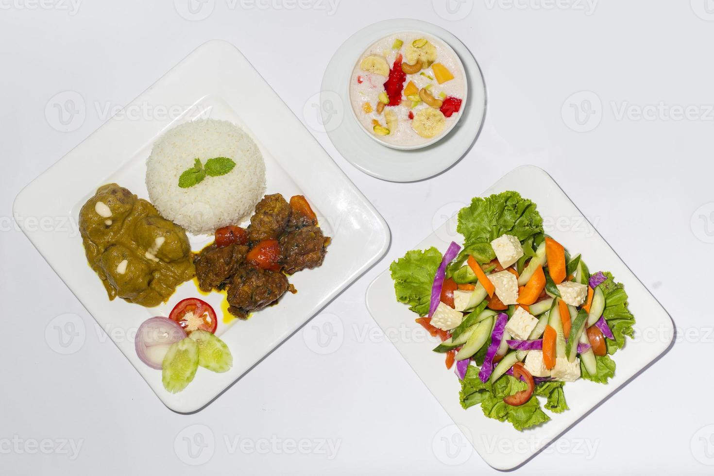 asiatico stile Ramadan Sehri cibo impostare. salutare pieno corso pasto. un' piatto di verde insalata, un' piatto di aereo riso e 2 genere di Manzo curry con faluda dessert su bianca sfondo. foto