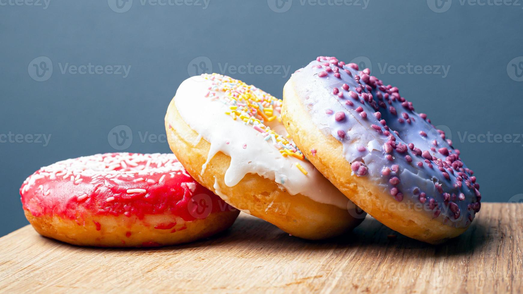 ciambelle con glassa multicolore rosso bianco e viola su un supporto di legno su uno sfondo grigio foto