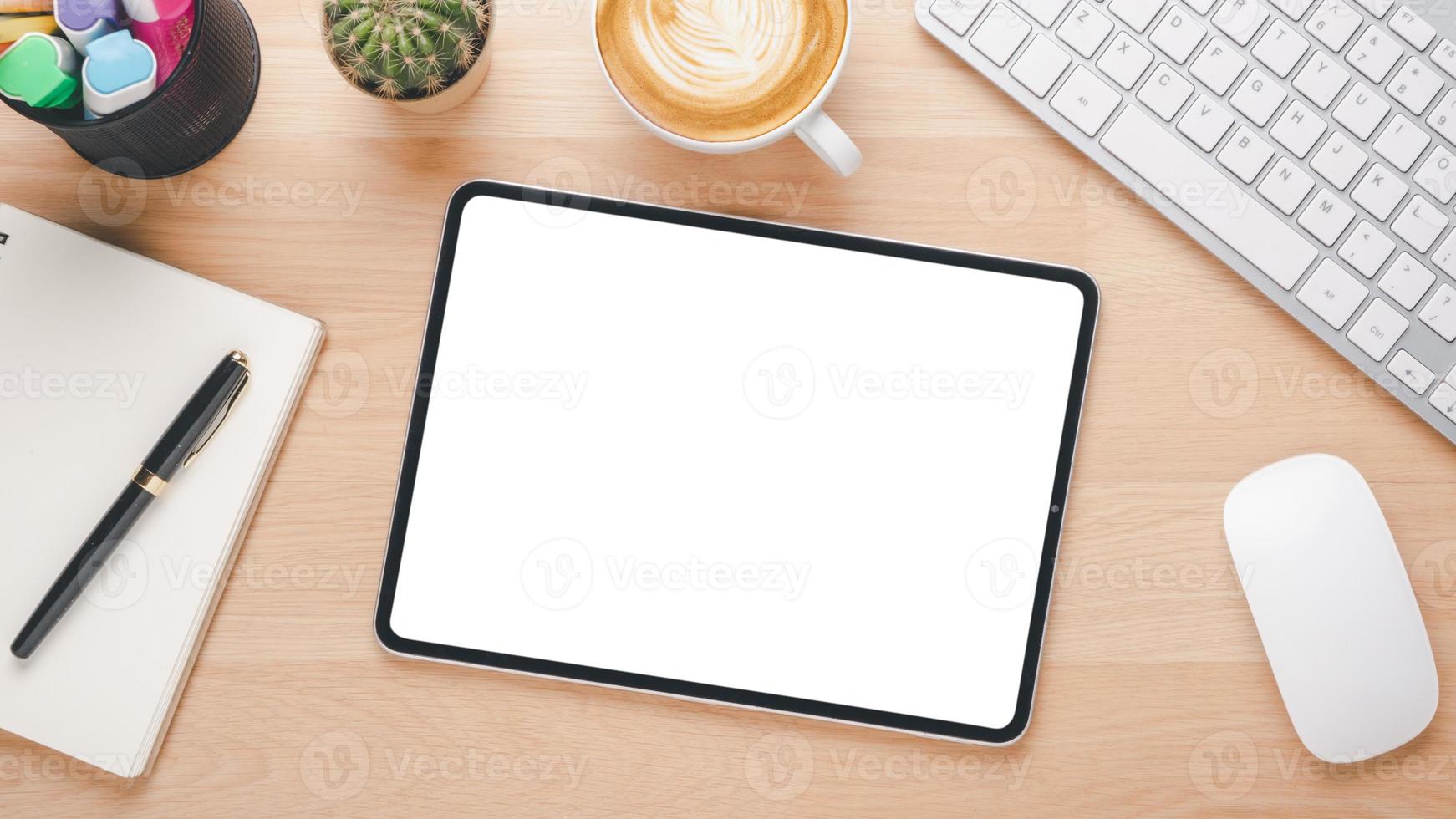 di legno scrivania posto di lavoro con vuoto schermo digitale tavoletta, tastiera computer, topo, penna, taccuino e tazza di caffè, superiore Visualizza piatto posizione. foto