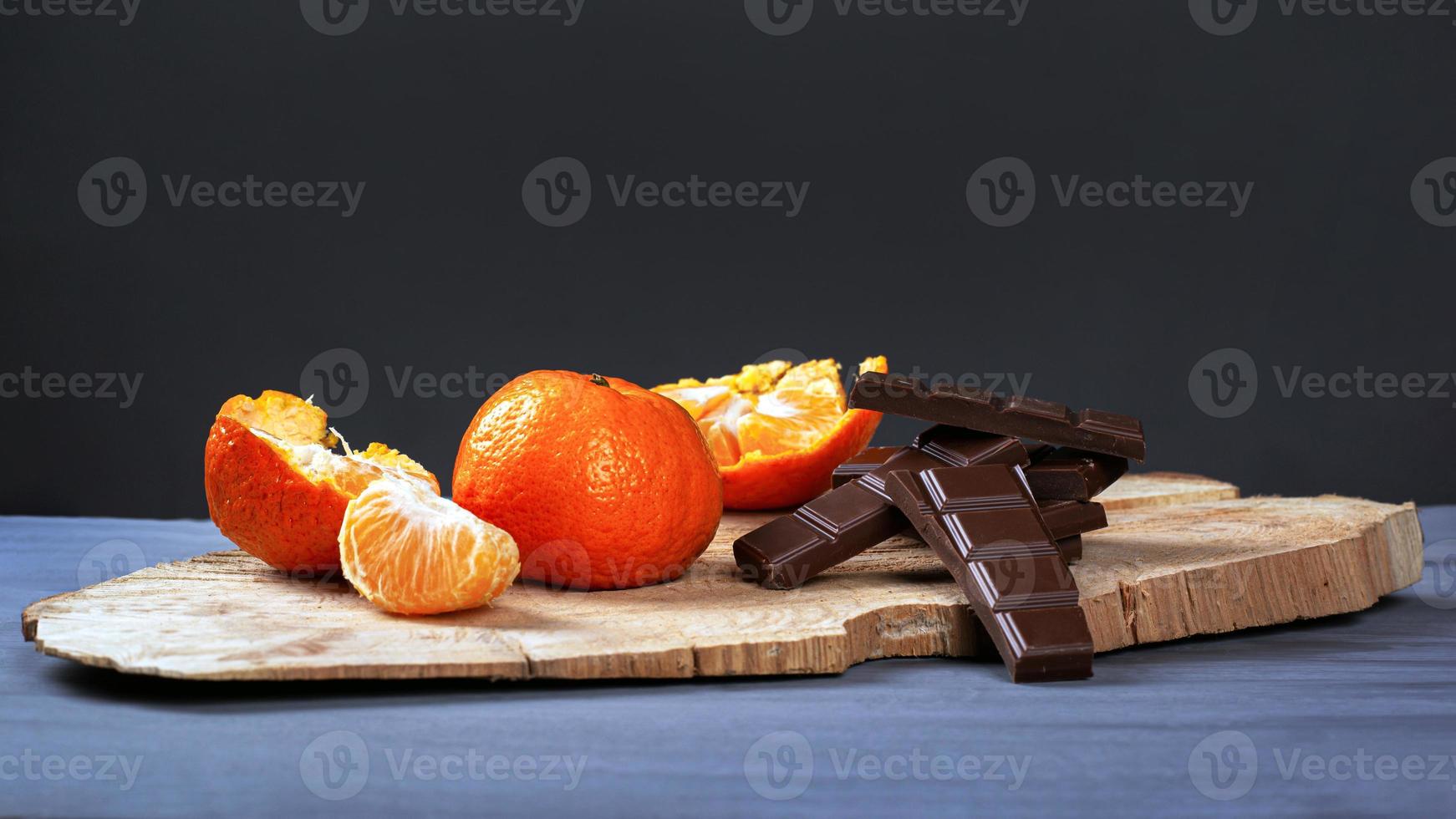 mandarini con cioccolato nero su supporto in legno su uno sfondo grigio scuro foto