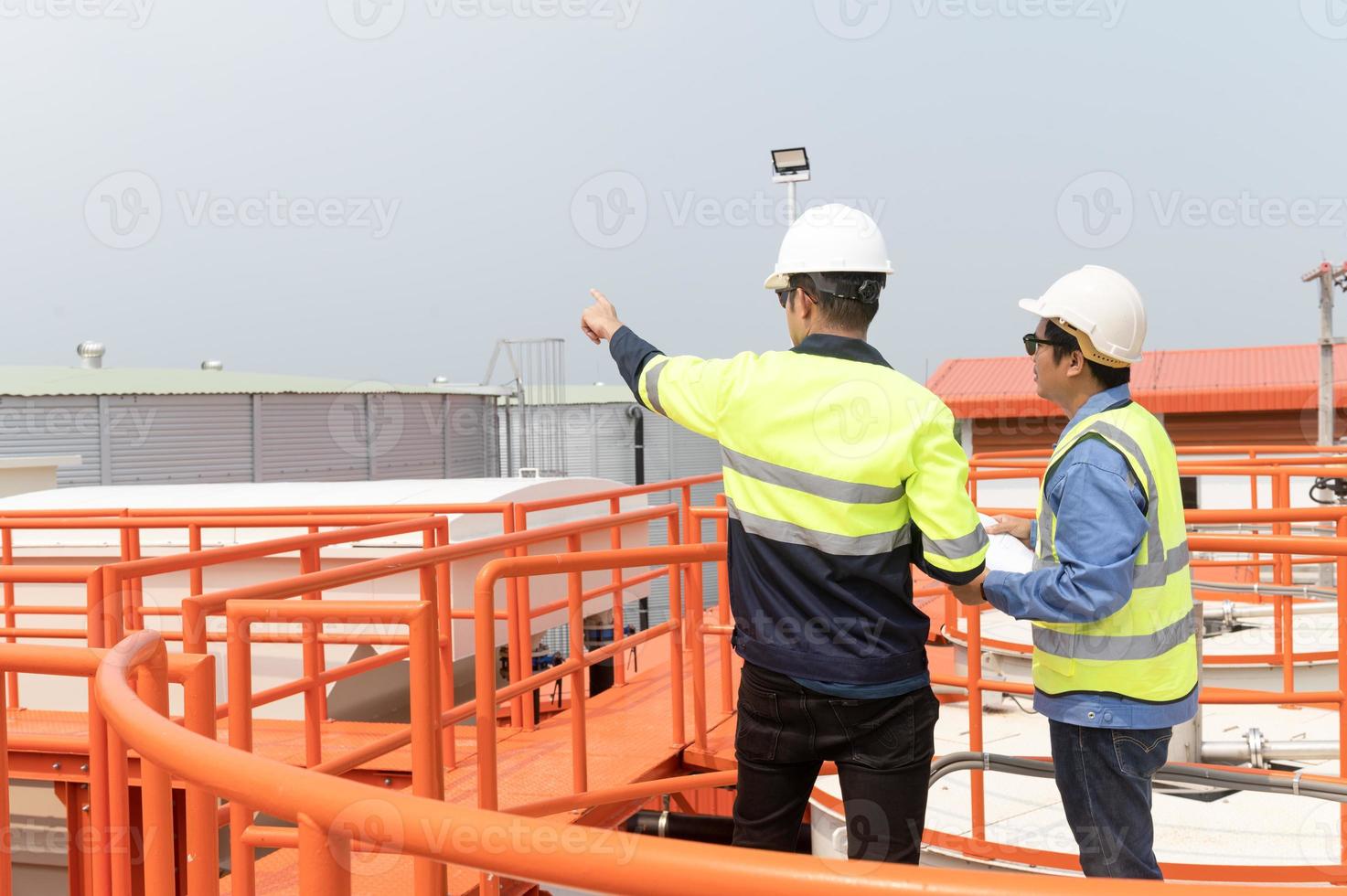 Due pesante industriale ingegneri in piedi nel un' standard acqua trattamento pianta uso digitale tavoletta computer e chattare. asiatico industria professionisti foto