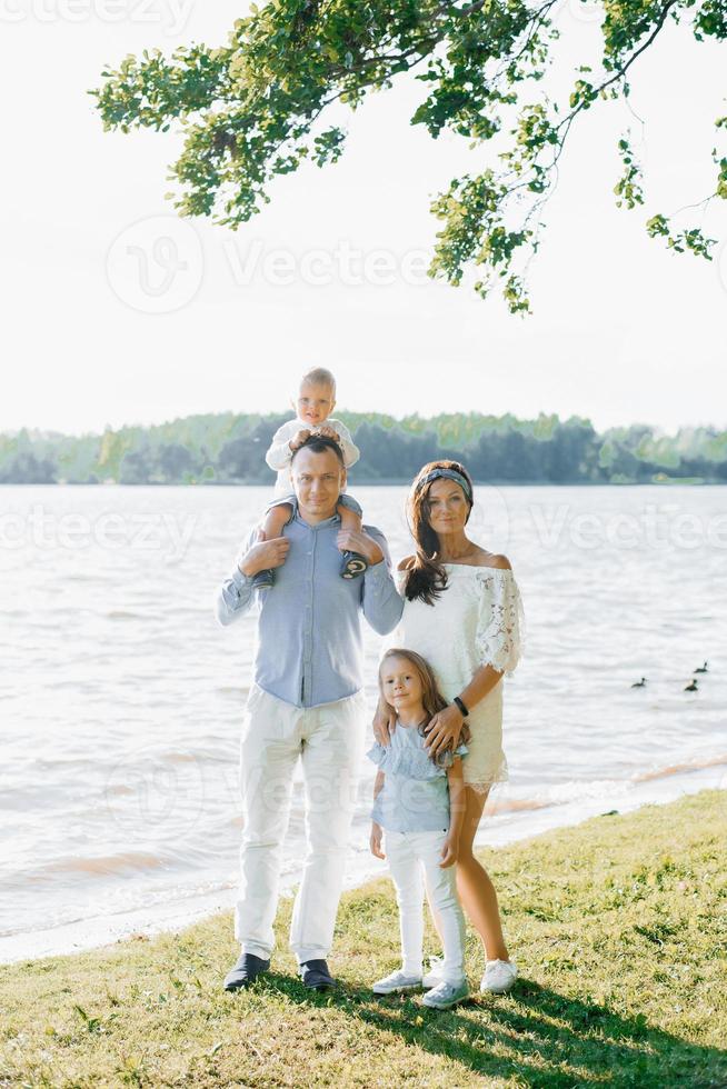 estate ritratto di un' bellissimo giovane famiglia con Due bambini vicino il lago. mamma, papà, figlio e figlia foto