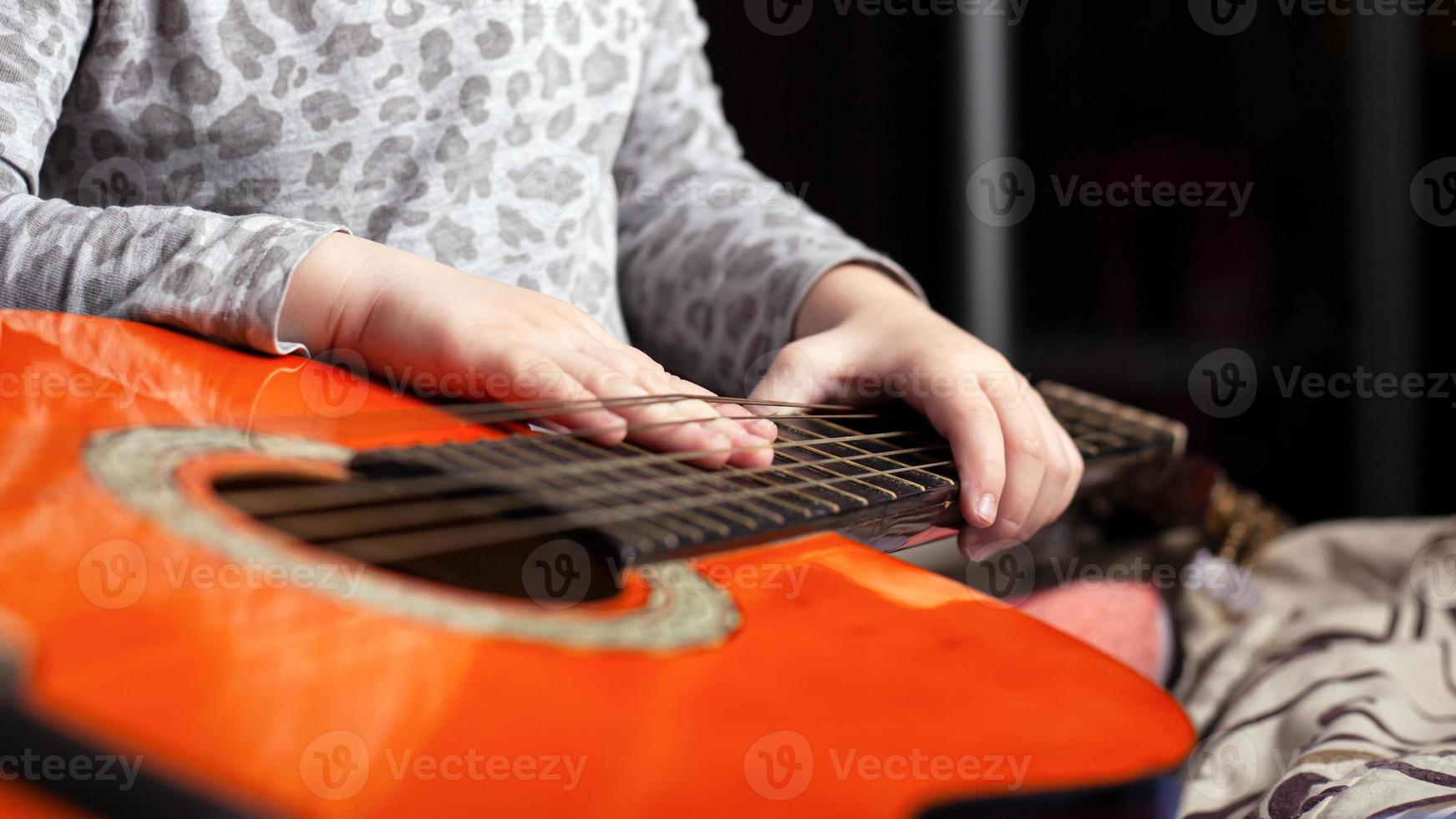 un bambino suona una chitarra acustica a sei corde di colore arancione foto