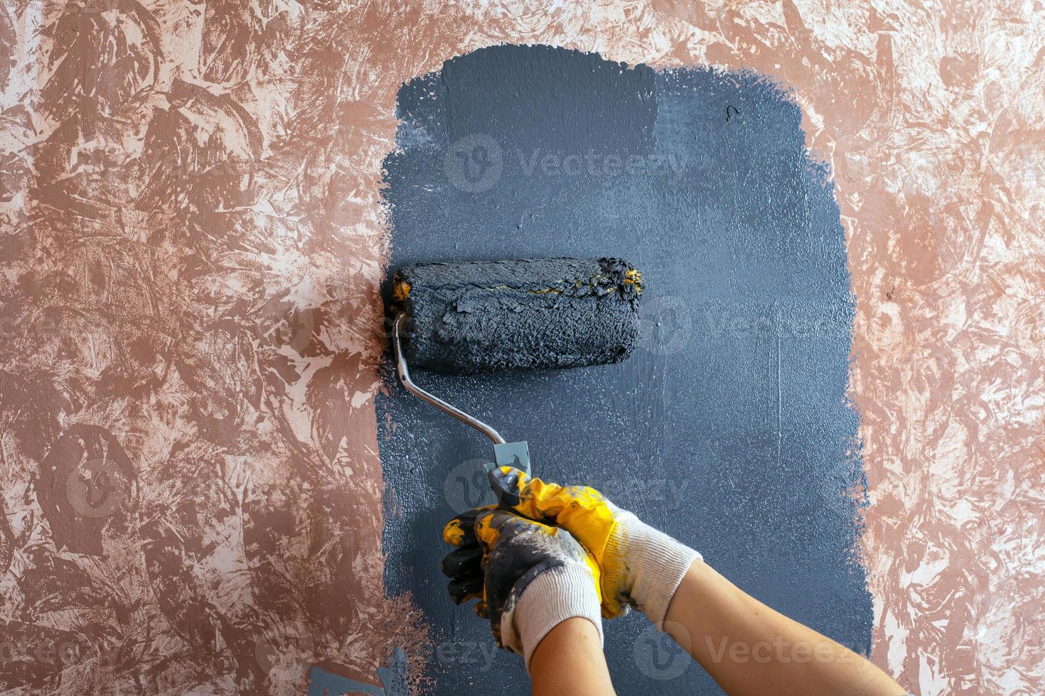 dipingere il muro con un rullo di vernice grigia foto