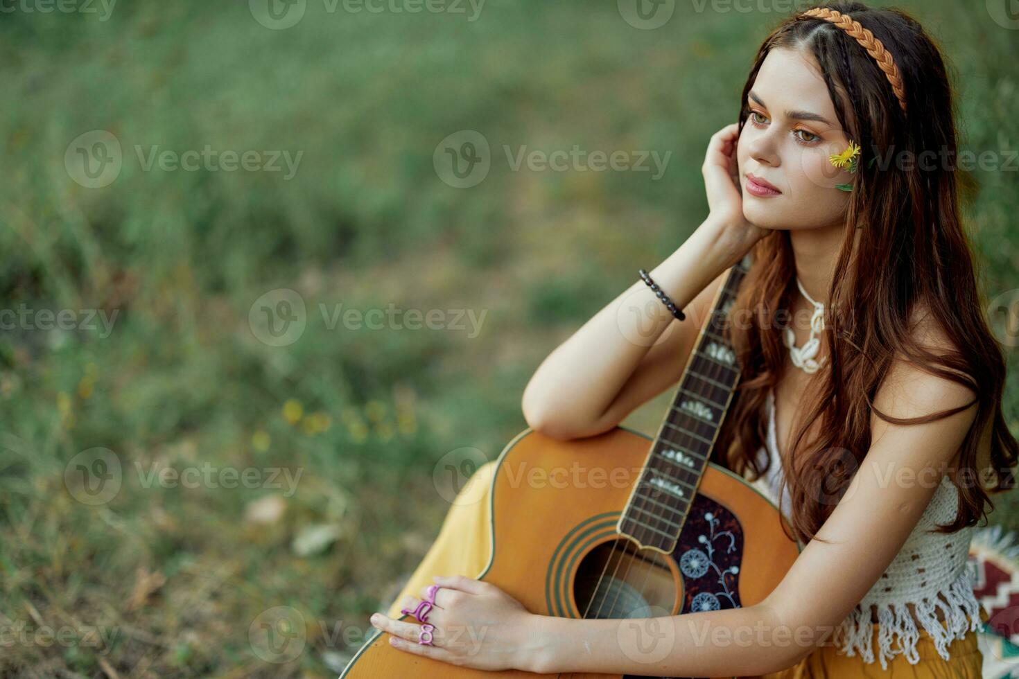 hippie eco amichevole donna con un' chitarra rilassante nel natura seduta su un' plaid di il lago nel il sera nel il raggi di il ambientazione sole. un' stile di vita nel armonia con il corpo e natura foto