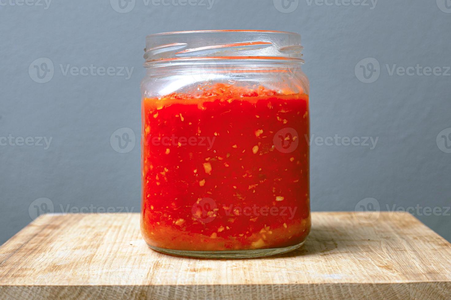 vaso con salsa adjika di pomodori su un tavolo in legno e uno sfondo grigio foto