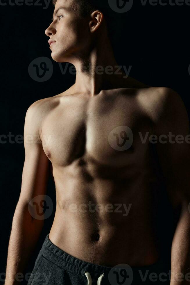 atleta con un' nudo torso guardare per il lato su un' nero sfondo ritagliata Visualizza foto