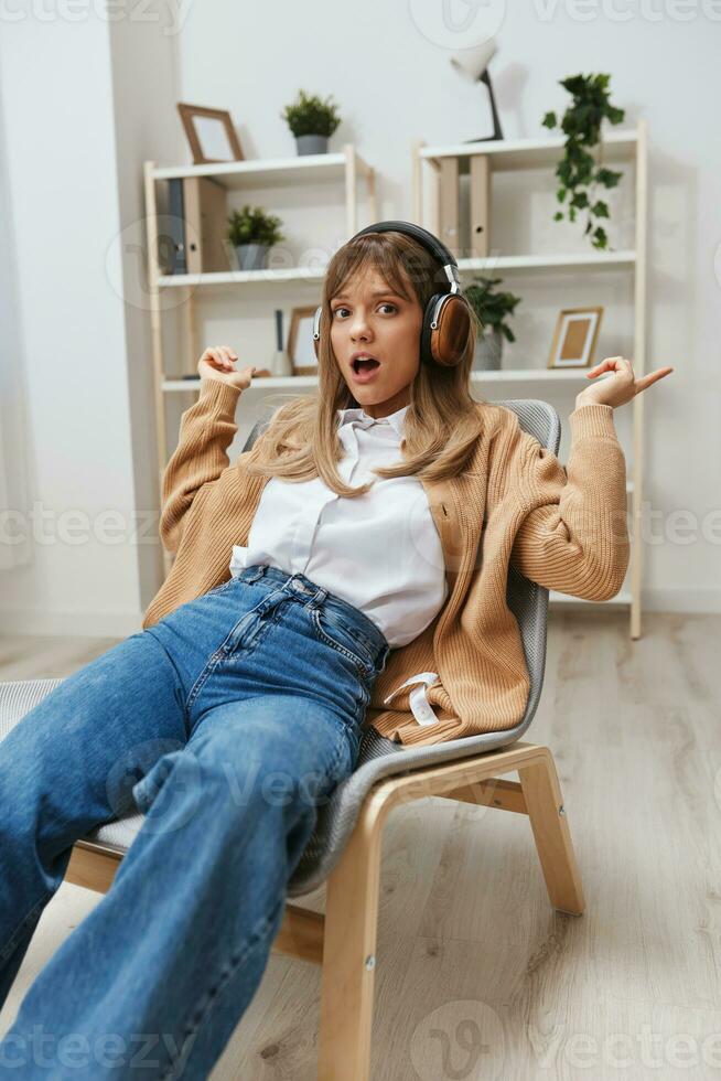 eccitato scioccato giovane bionda signora nel caldo maglione nel cuffie punto dita su apertura bocca ascolta preferito canzoni seduta nel poltrona a casa. musica tempo rilassante freddo elenco di riproduzione concetto. copia spazio foto