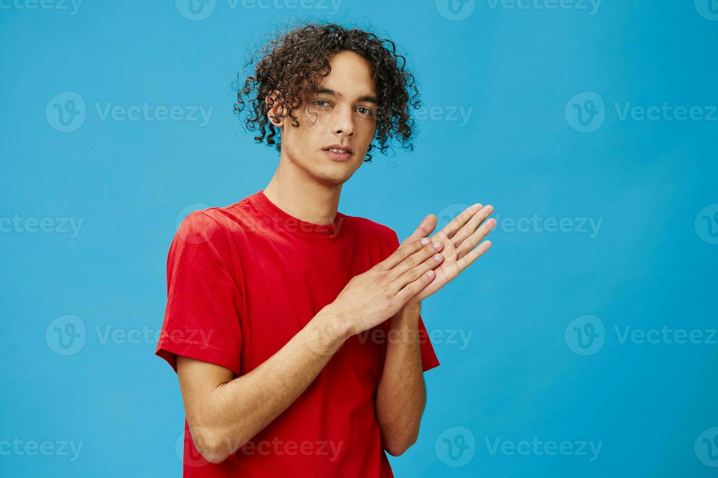 sornione Riccio abbronzato caucasico tipo nel di base rosso maglietta strofina il suo mani in posa isolato su al di sopra di blu sfondo. stile di vita e emozioni concetto. bene offrire con copia spazio per anno Domini foto