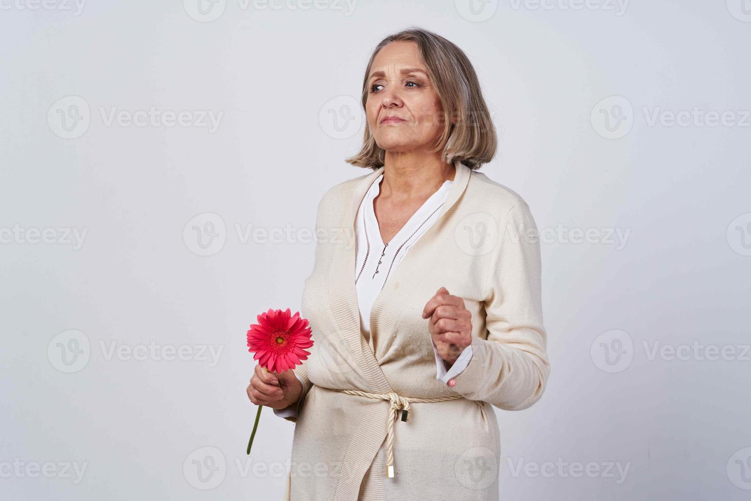 anziano donna nel un' accappatoio Tenere un' fiore regalo leggero sfondo foto