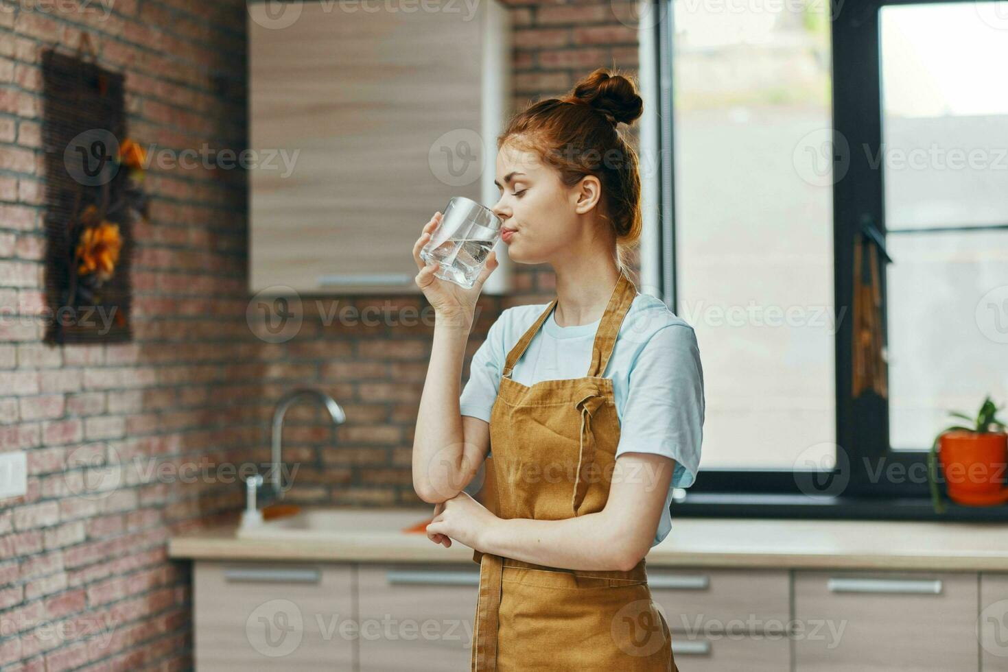 allegro donna potabile acqua nel un' Marrone grembiule cucina interno casa vita foto