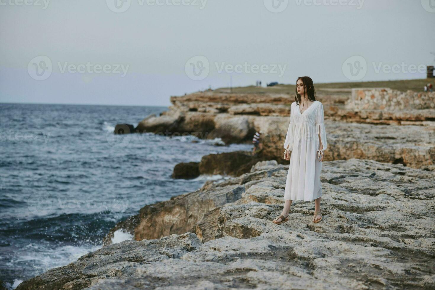 bella donna nel bianca vestito sta su il pietre spiaggia natura la libertà inalterato foto