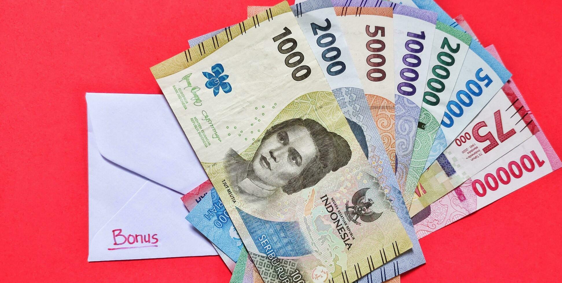 nuovo banconote rilasciato nel 2022 a partire dal rp.1,000 per rp.100,000. indonesiano rupia moneta con un' bianca Busta etichettato bonus. tunjangan hari raya concetto isolato su rosso sfondo. foto
