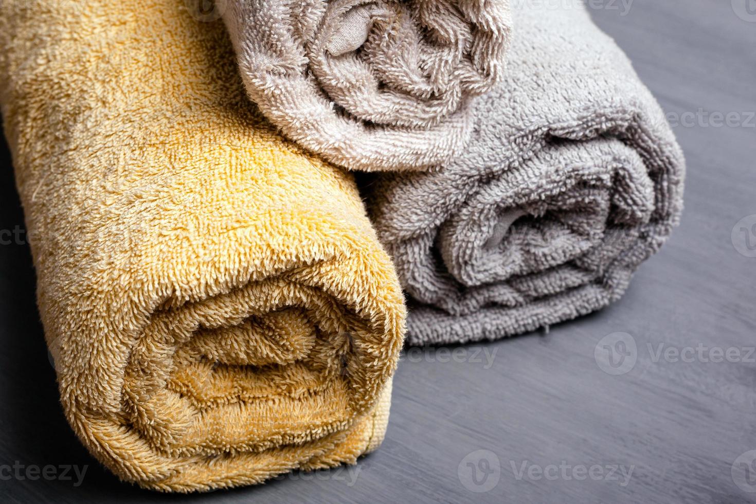 tre asciugamani piegati arrotolati color pastello su uno sfondo grigio foto