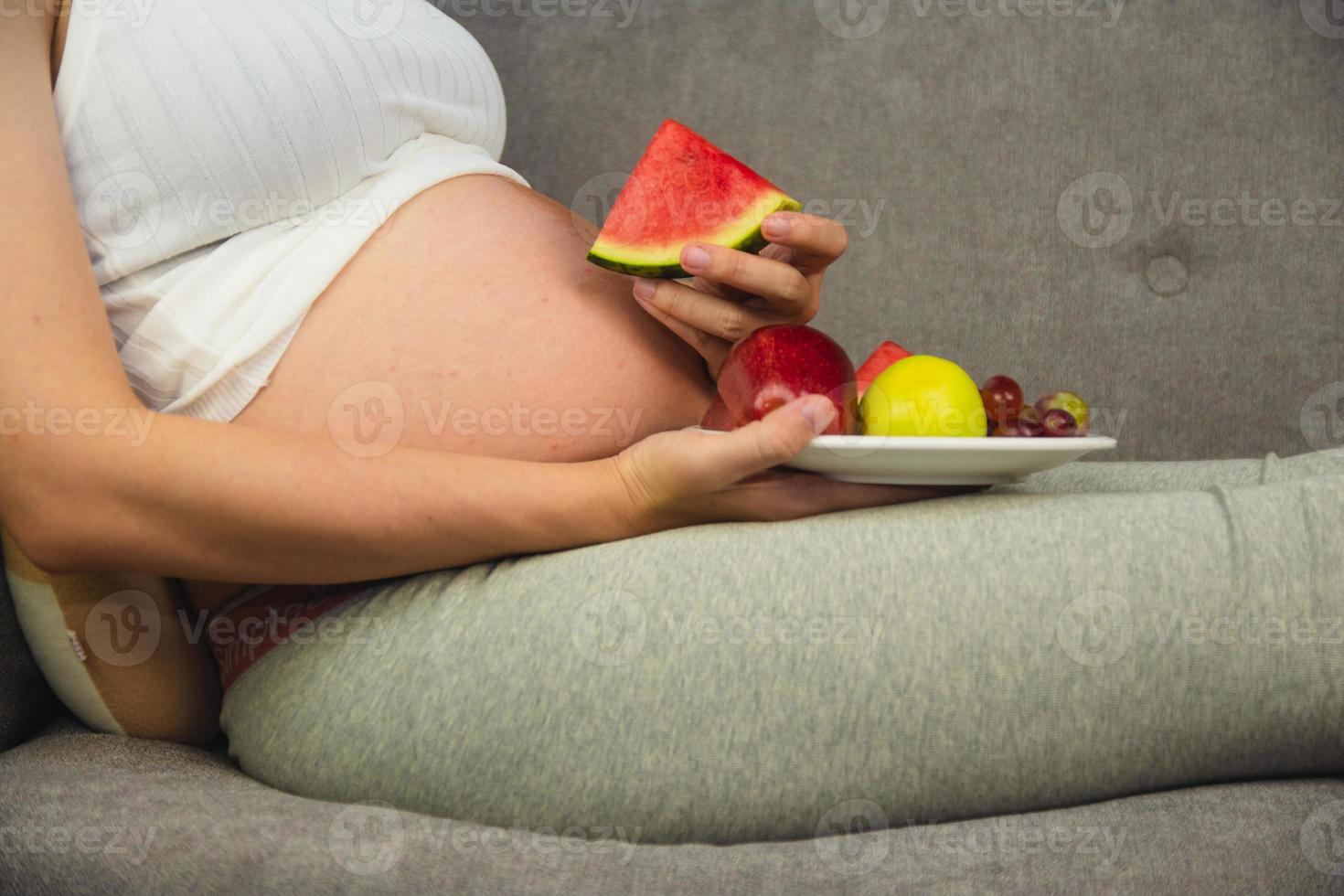 donna incinta mangia frutta anguria mela uva foto