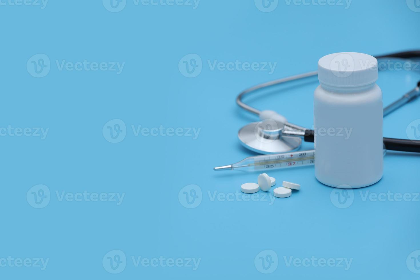 pillole fuoriuscita di pillola bottiglia siringa termometro e stetoscopio su sfondo blu foto
