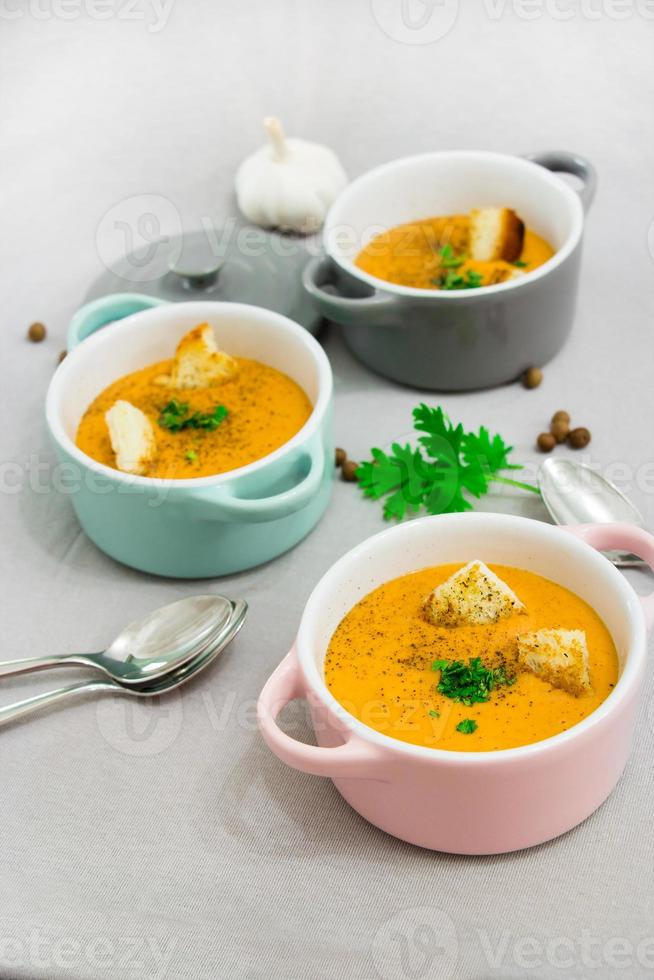 tre piccole pentole o ciotole con zuppa di crema di lenticchie rosse con fette biscottate, spezie ed erbe aromatiche, prezzemolo e coriandolo. su uno sfondo grigio chiaro. foto