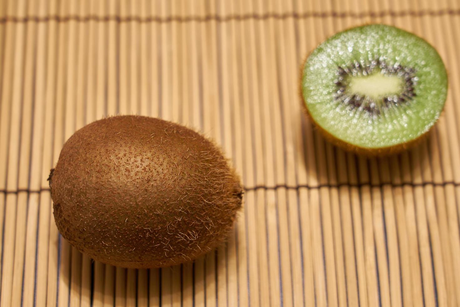 kiwi marrone maturo con kiwi verde tagliato su uno sfondo di paglia con spazio per il testo. foto