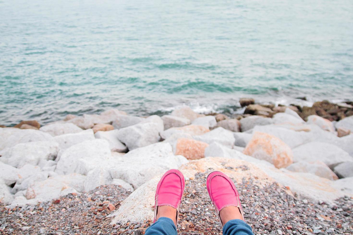 donne indossare rosa scarpe sedersi e rilassare su il spiaggia nel estate volta. foto