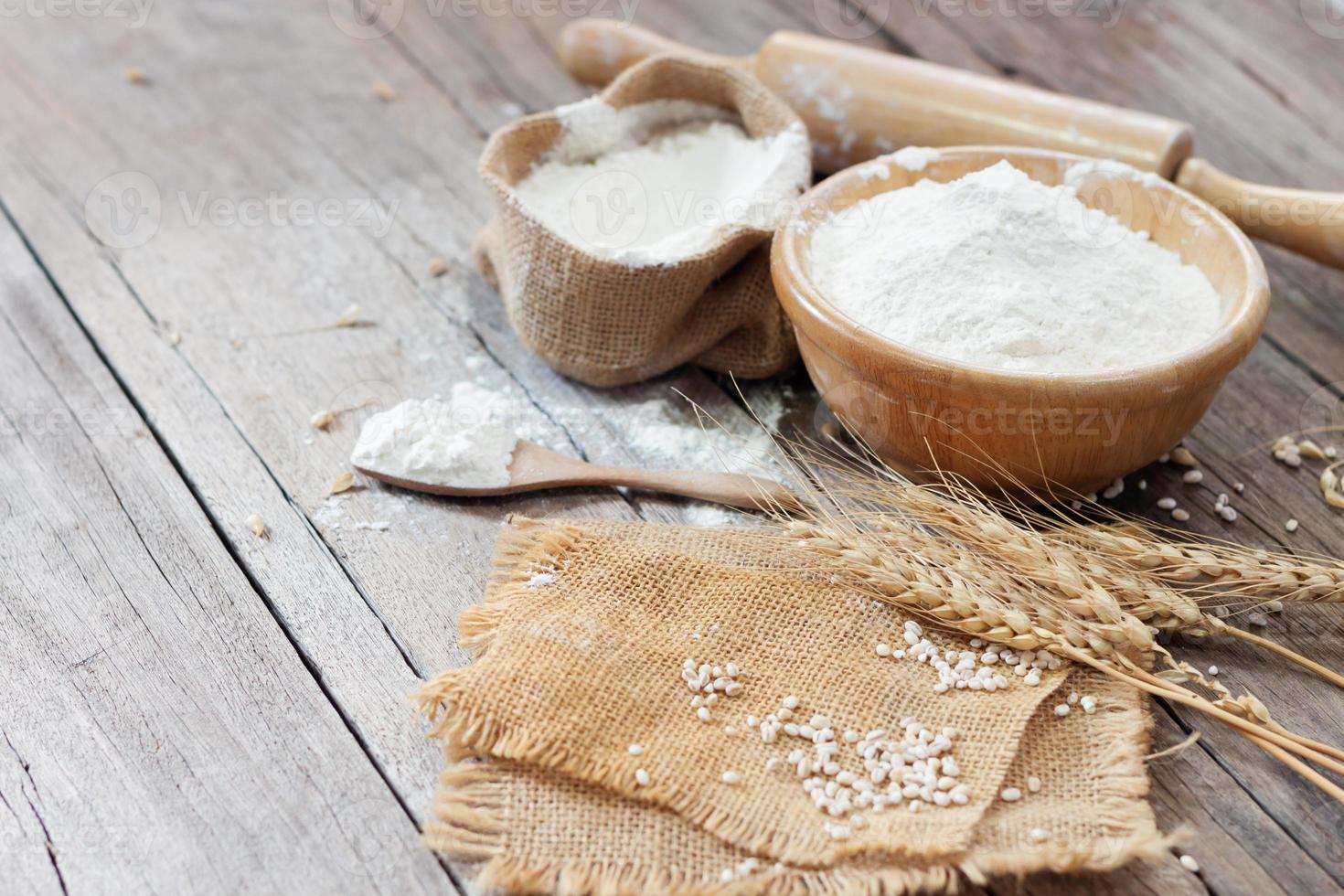 morbido messa a fuoco, Farina nel un' di legno ciotola, orecchie di Grano, orzo, cucinando, pane, e biscotti disposte su un' di legno tavolo nel un' rustico cucina, superiore Visualizza. foto