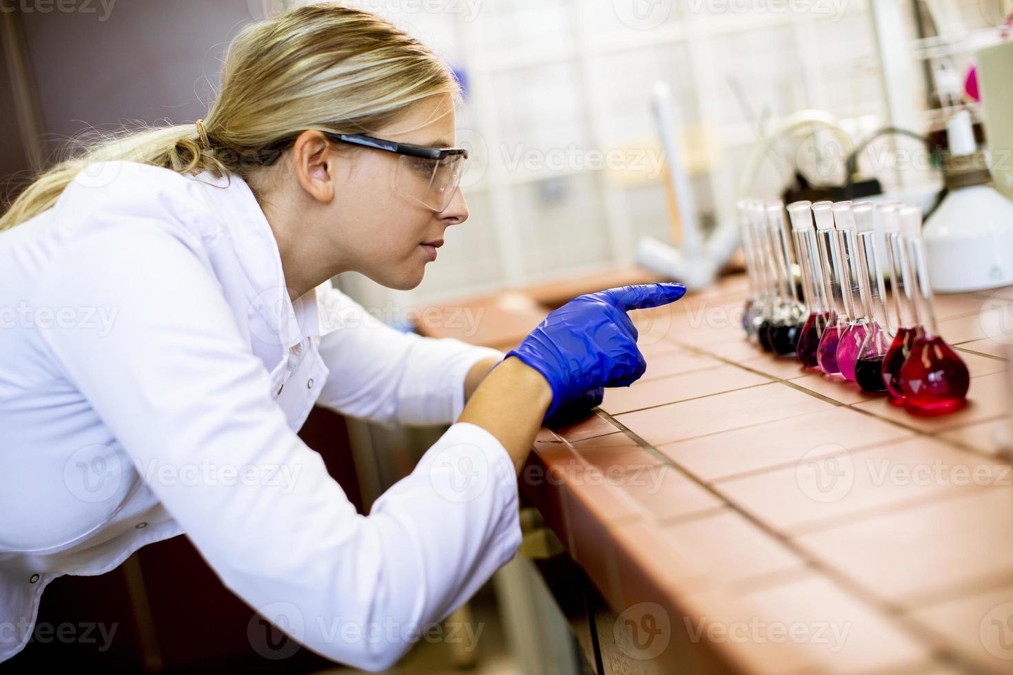 scienziato femminile in camice bianco analizzando campioni liquidi nel laboratorio biomedico foto