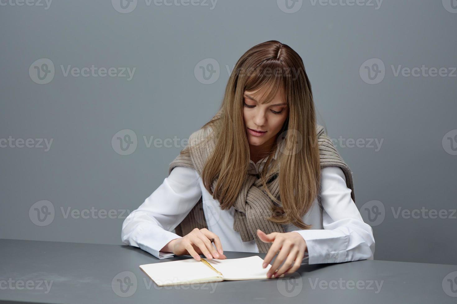 focalizzata giovane bionda alunno signora libero professionista nel caldo maglione leggere saggio utilizzando quaderno seduta a posto di lavoro nel grigio moderno casa ufficio. distanza formazione scolastica e carriera professione concetto. copia spazio foto