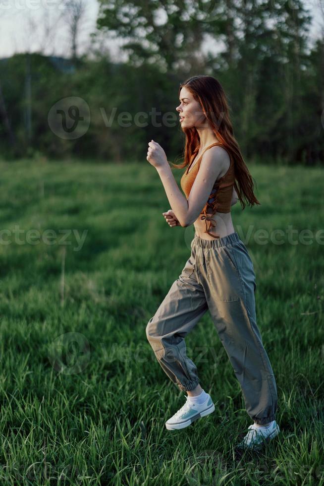 un' giovane donna esercizio al di fuori e in esecuzione nel il parco. nel il sera su il verde erba in il tramonto foto